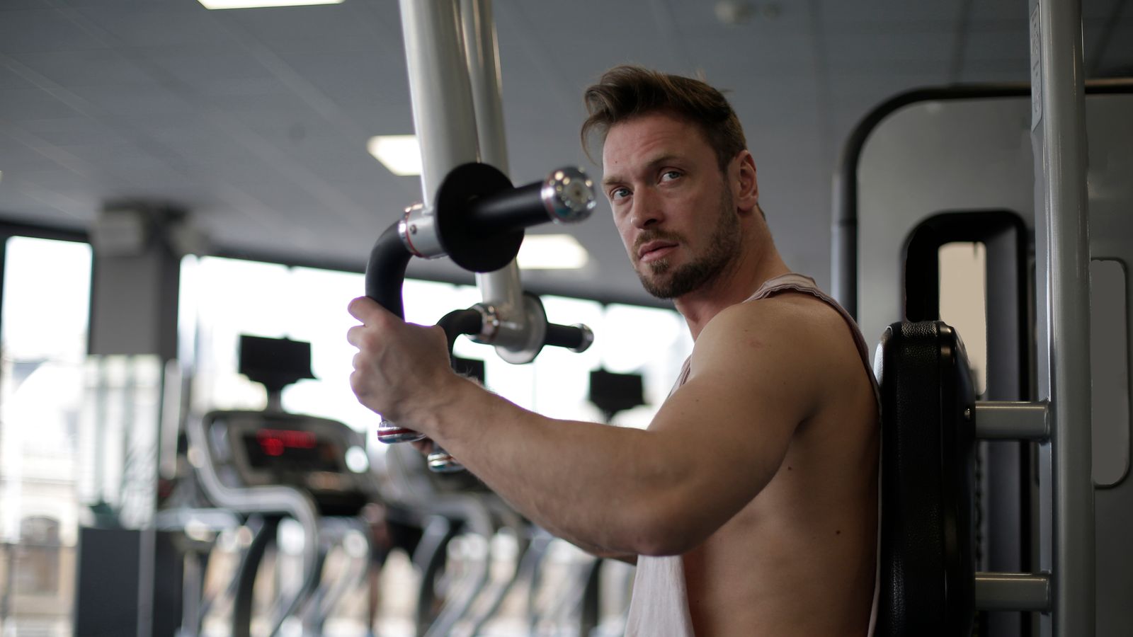 A man in his 30s finishing a set of deadlifts in a well-lit gym, calm editorial style
